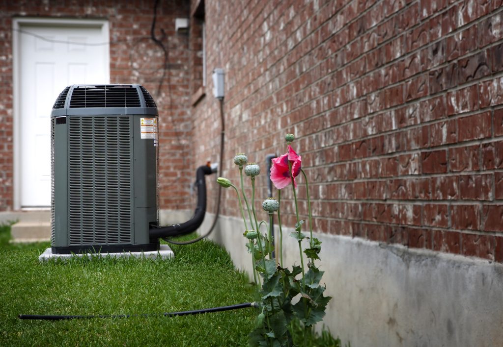 HVAC unit installed next to a brick home. Pink flowers in foreground.
